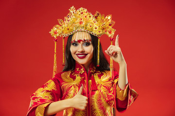 Chinese traditional graceful woman at studio over red background. Beautiful girl wearing national costume. Chinese New Year, elegance, grace, performer, performance, dance, actress, dress concept