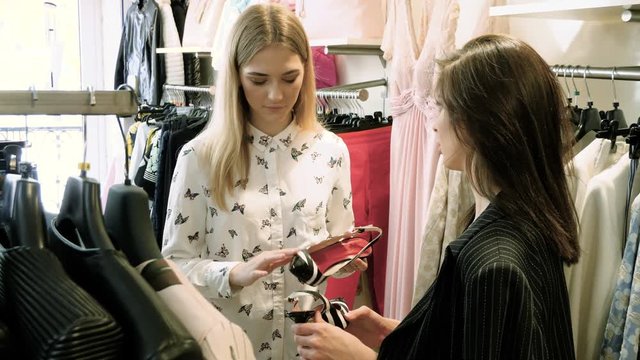 Two happy young girls are choosing clothes in a department store. 4K