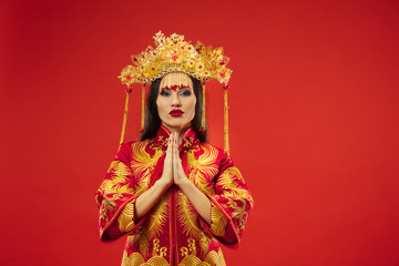 Chinese traditional graceful woman at studio over red background. Beautiful girl wearing national costume. Chinese New Year, elegance, grace, performer, performance, dance, actress, dress concept