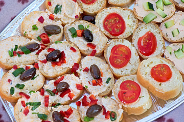 Variety of mini sandwiches with cheese cream, vegetables  roasted cherry tomatoes, olives, cucumber, spring onions, paprika, basil and other herbs. Fresh appetizer canape at the picnic outdoors.  