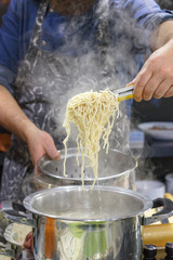 Chef takes out with slotted spoon hot steaming egg noodles from the pan
