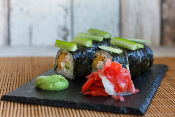Japanese rolls with cucumber, crabs and omelet on a black board with wasabi and ginger