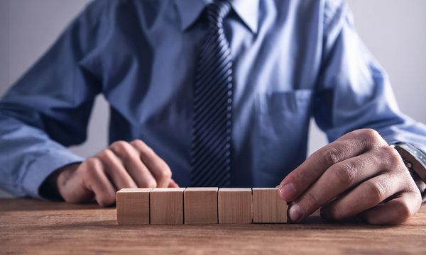 Businessman holding wooden cube on a wooden table.