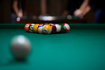 Sport billiard balls set arranged in shape of triangle on green billiard table in pub. Players are ready for the first hit of the round to start the billiard game.