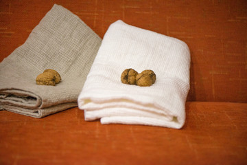 Fototapeta na wymiar Macro shot of rolled, folded snow white and grey natural linen sauna and bath towels next to small walnuts on orange background, on massage table. Beautiful home decor, gift for newlyweds for wedding 