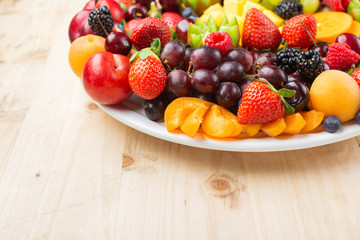 Healthy fruit platter, strawberries raspberries oranges plums apples kiwis grapes blueberries mango persimmon on wooden table, copy space for text, selective focus