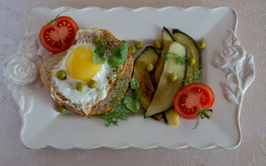 Dried egg on toast bread, eggplant, tomatoes and green peas as breakfast on white plate