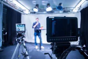 Journalist in a television studio is talking into a microphone, blurry film cameras