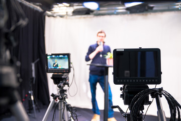 Journalist in a television studio is talking into a microphone, blurry film cameras
