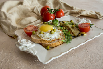 Dried egg on toast bread, eggplant, tomatoes and green peas as breakfast on white plate