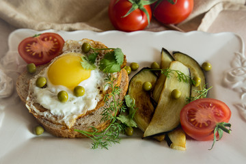 Fototapeta na wymiar Dried egg on toast bread, eggplant, tomatoes and green peas as breakfast on white plate