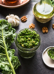 Green kale pesto in glass on dark rustic kitchen table background with ingredients, top view. Kale preparation. Healthy detox vegetables . Clean eating and dieting concept.