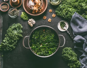 Poster Stewed kale in cooking pot on rustic kitchen table with ingredients for vegan kale recipes: nuts,garlic, olives oil, top view. Healthy meal.  Detox vegetables .  Clean eating and dieting concept. © VICUSCHKA