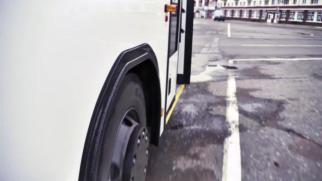 Side view of the white bus with bus wheel starting to move on grey asphalt background. Scene. Close up of white passenger bus and its wheel beginning to go, commercial transport wheels concept.