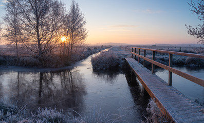 Small footbridge in the frozen Dutch countryside during winters dawn.