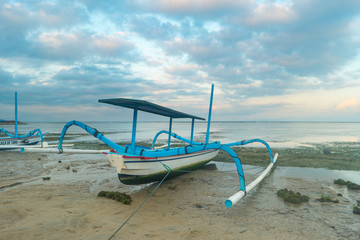 BALI, INDONESIA - SEPTEMBER 25, 2017: Traditional wooden boat at seashore with cloudy skies.