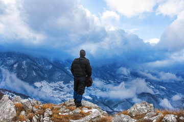 Hiker standing on a mountain top and looking into dynamic sky. Foggy mountain, Colorful winter landscape