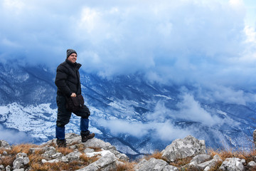 Fototapeta premium Hiker standing on a mountain top and looking into dynamic sky. Foggy mountain, Colorful winter landscape