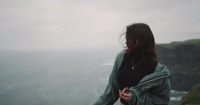 Beautiful young lady in the top of Cliffs moving slowly in front of the camera , she looks straight to the camere and smiling a bit dacing slow. 4k