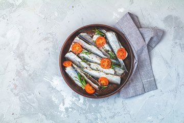 Sardines or baltic herring with parsley and tomatoes slices on ceramic plate