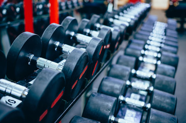 Fototapeta na wymiar Black metallic heavy dumbbells on stand in fitness gym