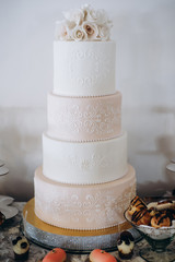a multi-level white wedding cake on a wooden table and pink flowers on top.