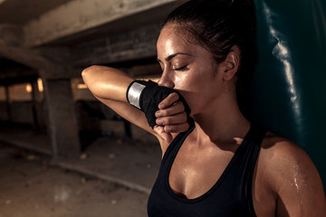 Female boxer resting after punching a boxing bag in warehouse. - Powered by Adobe