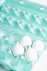 Four medium-size raw white eggs in a brightly-colored form-fitting styrofoam container.