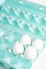 Obraz premium Four medium-size raw white eggs in a brightly-colored form-fitting styrofoam container.