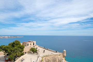 Panoramic view of city and Postiguet beach from Santa Barbara Castle in Alicante, Spain. Big palm trees in fortress on beautiful sea or ocean landscape in background, blue sky and tropical weather  