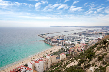 Panoramic view of Postiguet beach  from Santa Barbara Castle in Alicante, Spain. Sunny day at Mediterranean sea. Block apartment buildings in a row. Palm trees and vibrant blue water.  