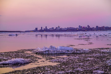 Obraz premium cracked ice on river in spring time during the sunset in pink and lilac colors with a cityscape on the horizon