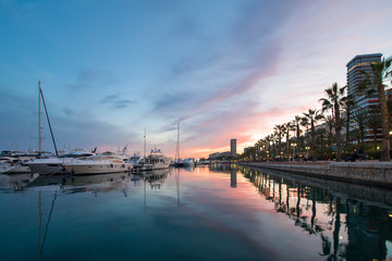 Fototapeta premium Beautiful port of Alicante, Spain at Mediterranean sea. Luxury yachts, ships, ferries and fishing boats sailing and standing in rows in harbor. Rich people traveling around the world. Sunset evening 