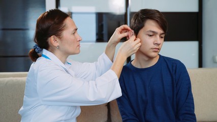 Woman doctor puts a hearing aid on a young guy.