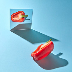 Half a ripe pepper is reflected in a mirror on a blue background with copy space and shadows....