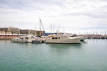 Fototapeta premium Beautiful port of Alicante, Spain at Mediterranean sea. Luxury yachts, ships, ferries and fishing boats sailing and standing in rows in harbor. Rich people traveling around the world. Sunny evening 