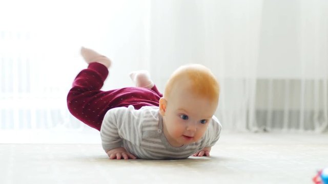 The baby girl learns to crawl, the first attempts to crawl. Baby crawls to the camera, smiling and laughing on the floor in the white room