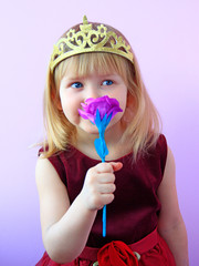Cute girl with crown on head smelling pink rose.Child in beautiful dress smiling
