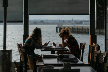 Silhouette of girls seating in a cafe near a pier