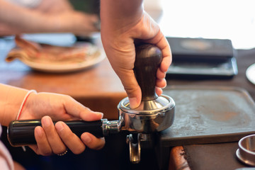 Asian woman barista presses ground coffee using tamper into portafilter , close up hands.