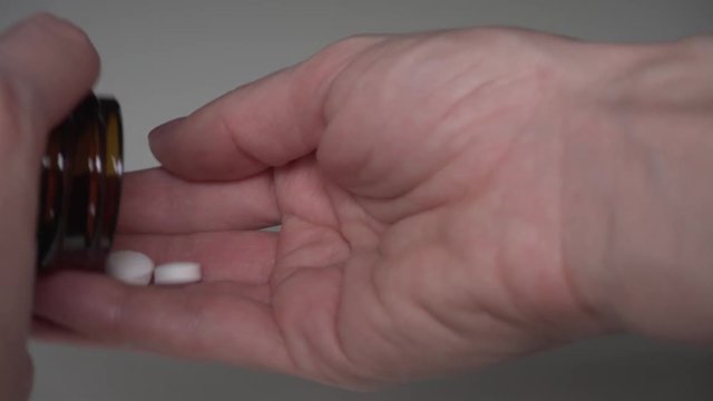 Taking two white pills from the jar. Pills being taken out from the bottle into the hand