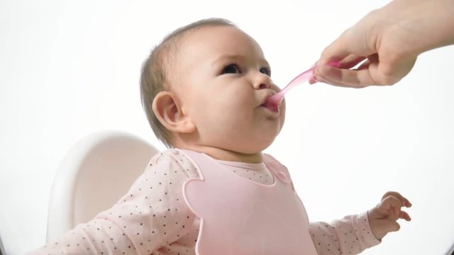 mother gives baby food from a baby spoon slow motion white