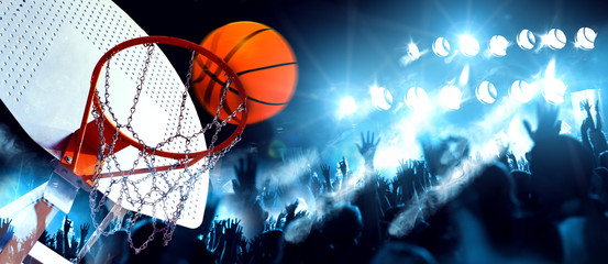 Deportes y entretenimiento. Baloncesto y deportes de equipo.Canasta  y pelota iluminados por los focos. Partido y evento deportivo. Público y multitud aplaudiendo el partido de baloncesto.