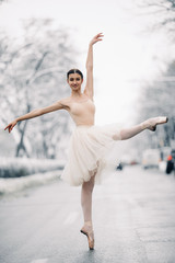 Beautiful ballerina is dancing on street of snowy city.