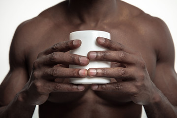 African man with white cup of tea or coffee, isolated on white studio background. Close up portrait in minimalism style of a young naked happy afro man