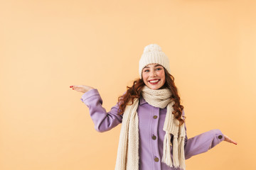 Portrait of european girl 20s in winter clothes smiling, while standing isolated over beige...