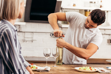 handsome boyfriend opening wine bottle near attractive girlfriend