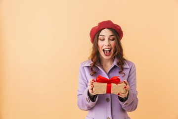 Image of gorgeous woman 20s with long hair smiling and holding present box, standing isolated over...