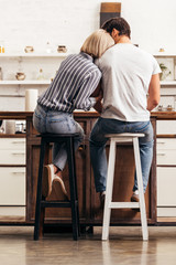 Fototapeta premium back view of boyfriend and girlfriend sitting on chairs in kitchen