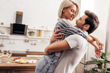 handsome boyfriend and attractive girlfriend hugging and smiling in kitchen